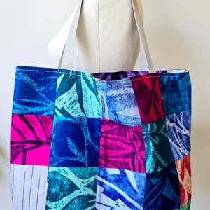 May include: A patchwork tote bag with a variety of blue, green, pink, and red floral patterns. The bag has two white straps.
