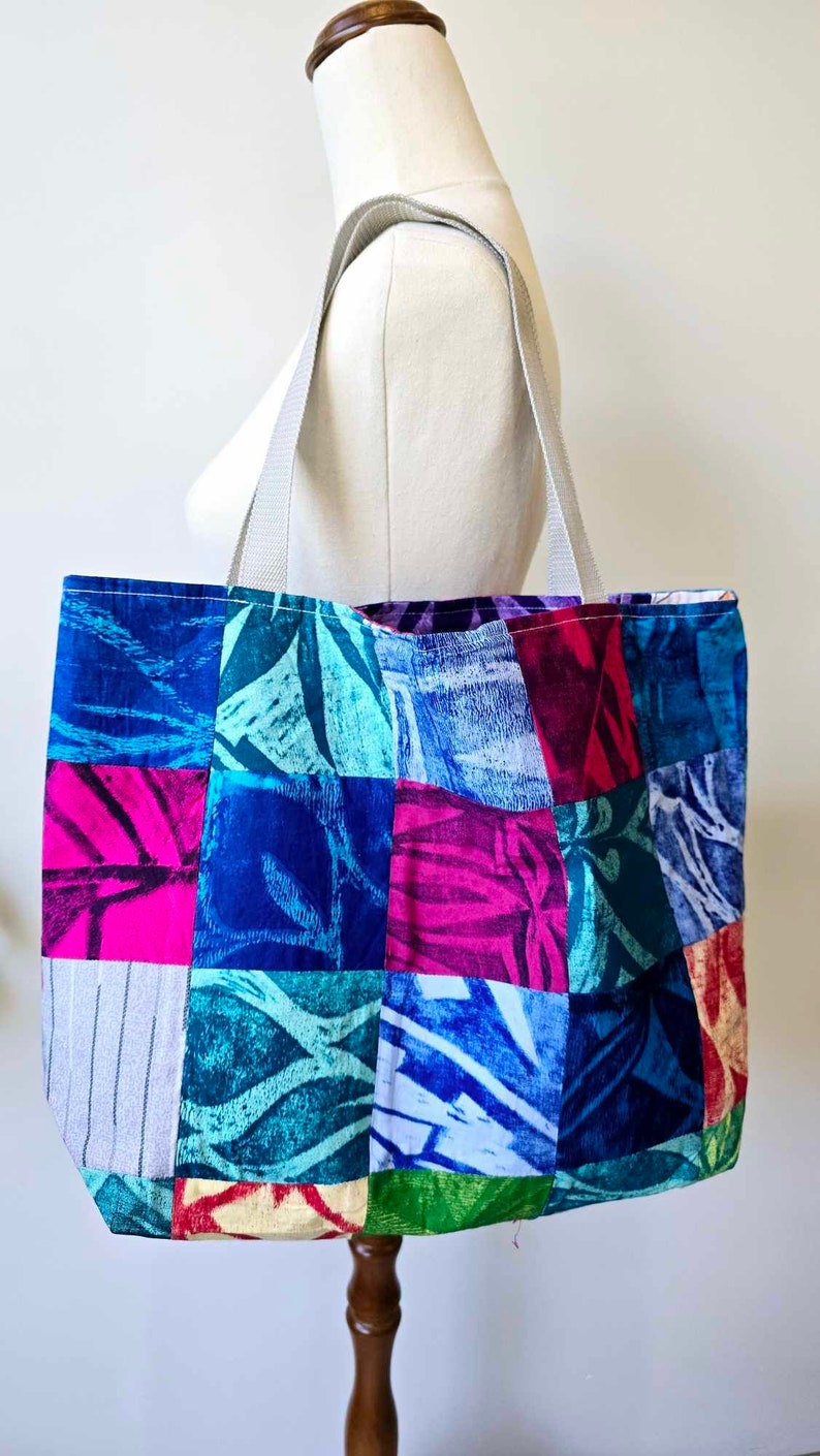 May include: A patchwork tote bag with a variety of blue, green, pink, and red floral patterns. The bag has two white straps.