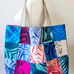 May include: A patchwork tote bag with a variety of blue, pink, green, and white floral patterns. The bag has two white straps.