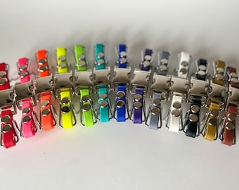 May include: A collection of colorful dog collar buckles in various shades, including red, orange, yellow, green, blue, purple, and brown. Each buckle has a silver metal clasp and matching leather strap, showcasing a range of vibrant hues.