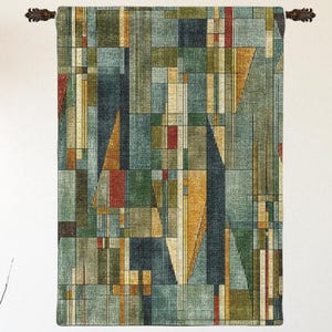 May include: A rectangular wall hanging featuring a geometric pattern of intersecting lines and blocks in shades of teal, olive green, mustard yellow, and deep red. The textile is suspended from a dark horizontal rod with decorative end caps.