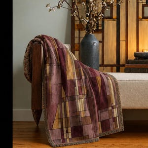 May include: A beige upholstered bench with wooden arms and legs, draped with a maroon and gold geometric patterned throw blanket. Behind the bench stands a tall, rectangular wooden screen with stained glass panels and a dark gray vase with branches.