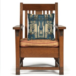 May include: A square throw cushion featuring a geometric pattern in shades of blue, cream, and green, placed on a dark brown wooden armchair with a slatted back and a solid seat cushion upholstered in a muted orange fabric with a subtle texture.