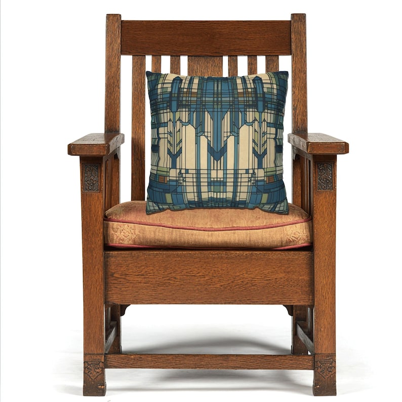 May include: A square throw cushion featuring a geometric pattern in shades of blue, cream, and green, placed on a dark brown wooden armchair with a slatted back and a solid seat cushion upholstered in a muted orange fabric with a subtle texture.
