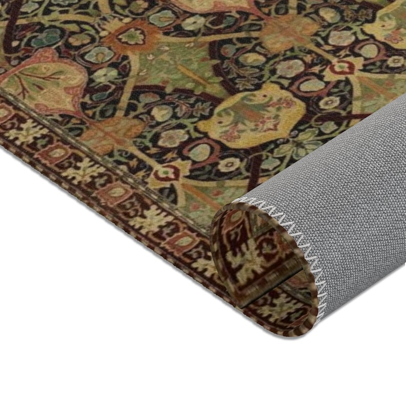 Puede incluir: Una alfombra enrollada con un dise&ntilde;o estampado en marr&oacute;n oscuro, verde y dorado. La alfombra tiene un borde con flecos y est&aacute; enrollada sobre un respaldo gris.