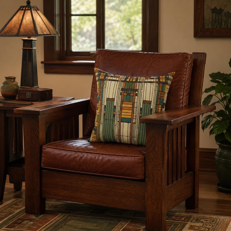 May include: A square throw pillow featuring a geometric pattern of vertical lines and rectangular blocks in shades of cream, forest green, mustard yellow, and dark brown, resting on a dark brown leather armchair with a wooden frame.