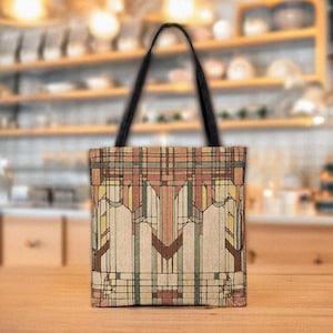 May include: A tote bag with a geometric pattern in shades of brown, beige, yellow, and green. The bag has a black handle and a rectangular shape. The design appears to be inspired by an architectural style.