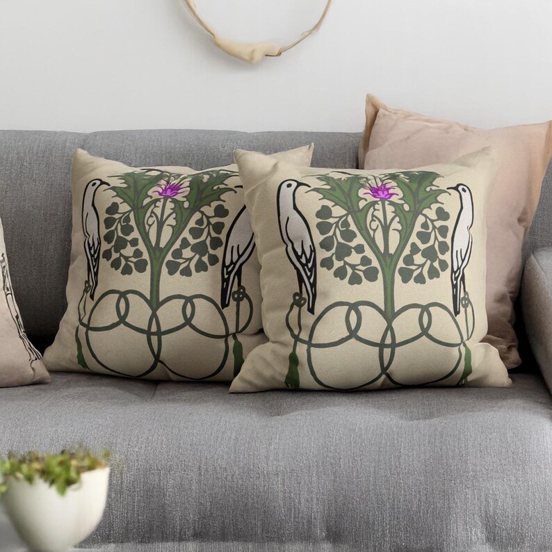 Pu&ograve; includere: Due cuscini quadrati con sfondo color crema e una stampa botanica simmetrica. Il design mostra due uccelli bianchi rivolti verso una pianta centrale verde con un fiore viola, accentuato da linee intrecciate di colore verde scuro.