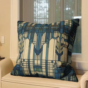 May include: A square throw cushion featuring a geometric pattern in shades of navy blue, light blue, cream, and sage green. The design consists of intersecting vertical and horizontal lines forming a complex grid with symmetrical architectural shapes.