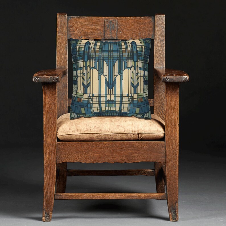 May include: A square throw cushion featuring a geometric pattern in shades of blue, cream, and brown, resting on a dark brown wooden armchair with a light tan seat cushion. The cushion design consists of vertical lines and angular shapes.
