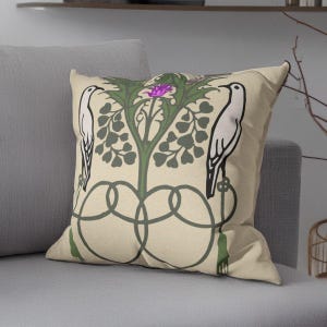 Pu&ograve; includere: Un cuscino quadrato con sfondo beige caratterizzato da un design grafico simmetrico. Due uccelli bianchi sono rivolti verso una pianta verde centrale con un fiore viola. Il disegno include linee intrecciate verde scuro e nappe.