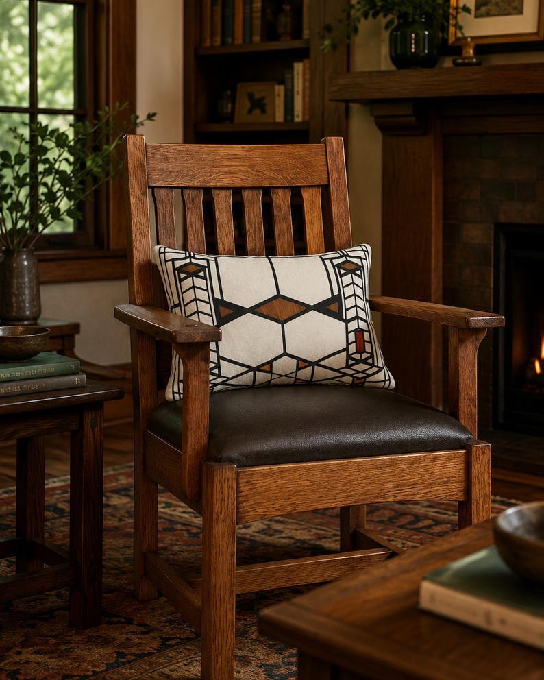 May include: A wooden armchair with a dark brown leather seat and a high slatted backrest. A rectangular throw pillow rests on the seat, featuring a cream-colored fabric with a geometric pattern in black, brown, and small accents of red.