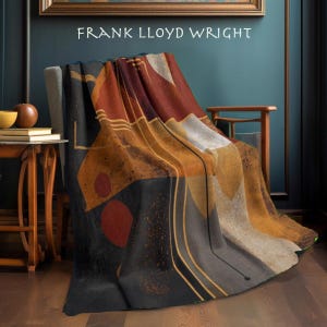 May include: A throw blanket with an abstract design in shades of black, brown, orange, and gray, draped over a chair. The blanket features a geometric pattern with circular and linear elements. The text "FRANK LLOYD WRIGHT" is visible at the top.