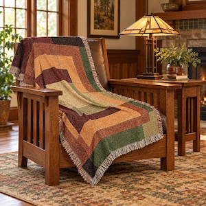 May include: A woven throw blanket featuring a geometric pattern of nested rectangles in shades of deep burgundy, burnt orange, olive green, and tan. The blanket has a textured finish with fringed edges and is draped over a wooden armchair.