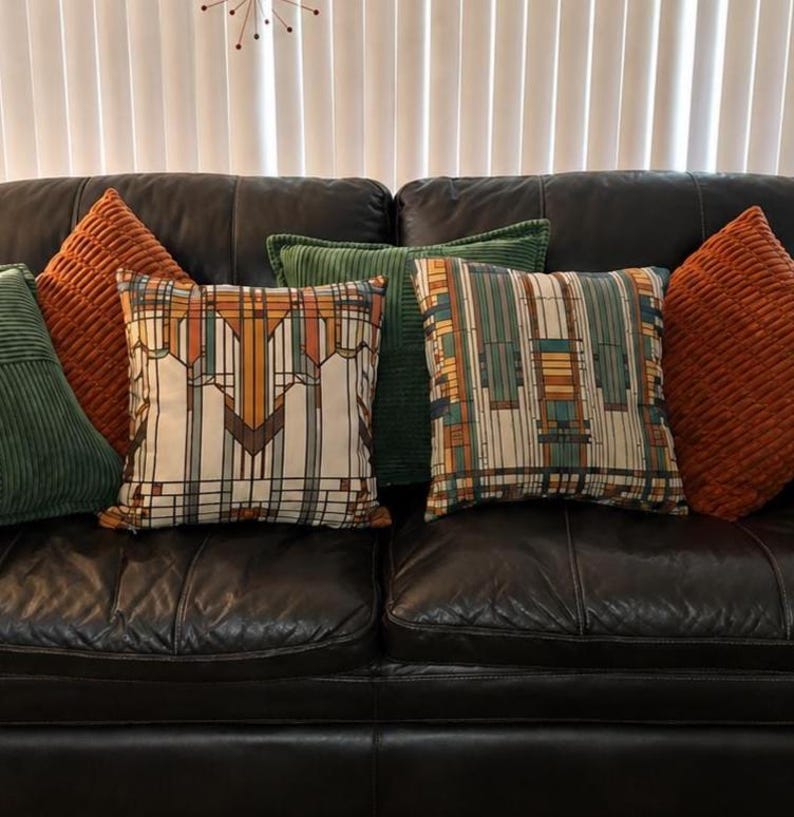 May include: A collection of square throw pillows arranged on a dark leather sofa. The set includes two solid orange corduroy pillows, two solid green corduroy pillows, and two pillows featuring a geometric pattern in shades of orange, green, and tan.