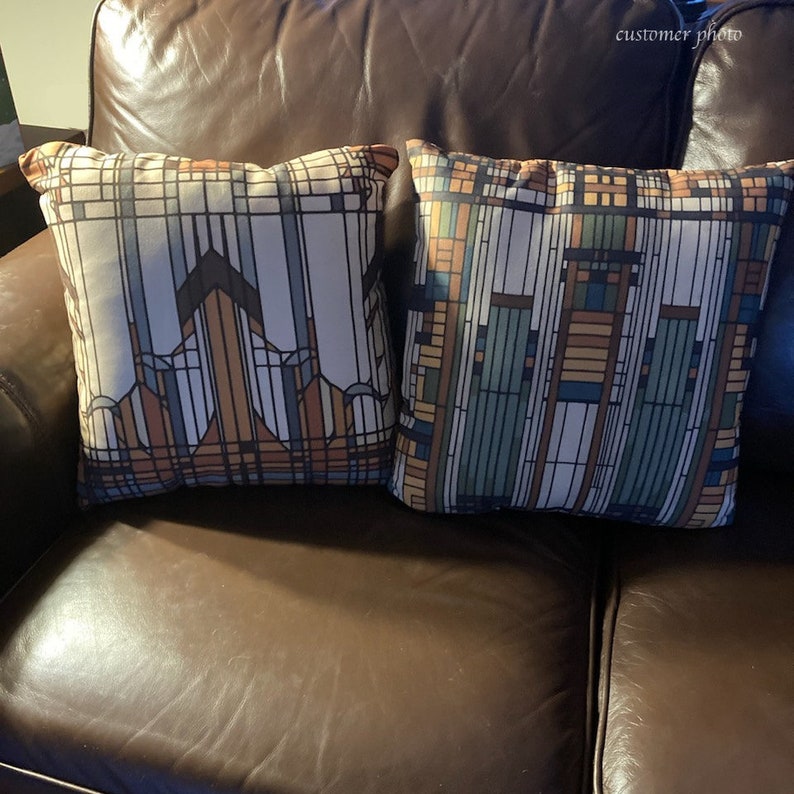 May include: Two square throw pillows featuring a geometric stained glass pattern. The left pillow displays brown, tan, and dark blue lines. The right pillow features a vertical arrangement of green, blue, tan, and brown rectangular segments.