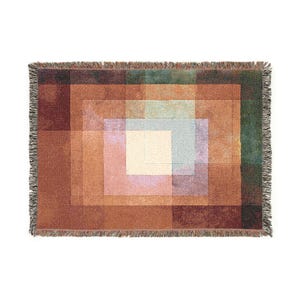 以下が含まれることがあります： 幾何学模様の織りスローケット。茶色、オレンジ、緑、青の色合いの入れ子になった正方形が特徴です。端はフリンジで仕上げられています。