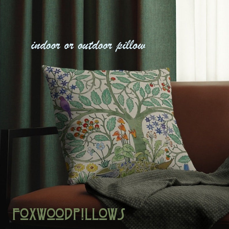 May include: A decorative pillow with a colorful tree and floral pattern. The pillow is on a brown couch with a green throw blanket. The text "indoor or outdoor pillow" is above the pillow. The text "FOXWOODP!LLOWS" is below the pillow.