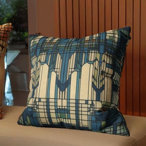 May include: A square throw cushion featuring a geometric pattern with intersecting lines and blocks in shades of navy blue, light blue, cream, and muted green. The design consists of vertical and horizontal lines forming a grid-like structure.