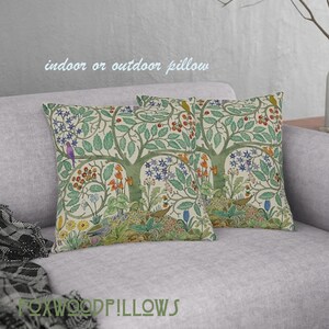 May include: Two decorative throw pillows with a floral pattern featuring a tree with birds and flowers. The pillows are on a light gray couch. The text "indoor or outdoor pillow" is visible at the top of the image.