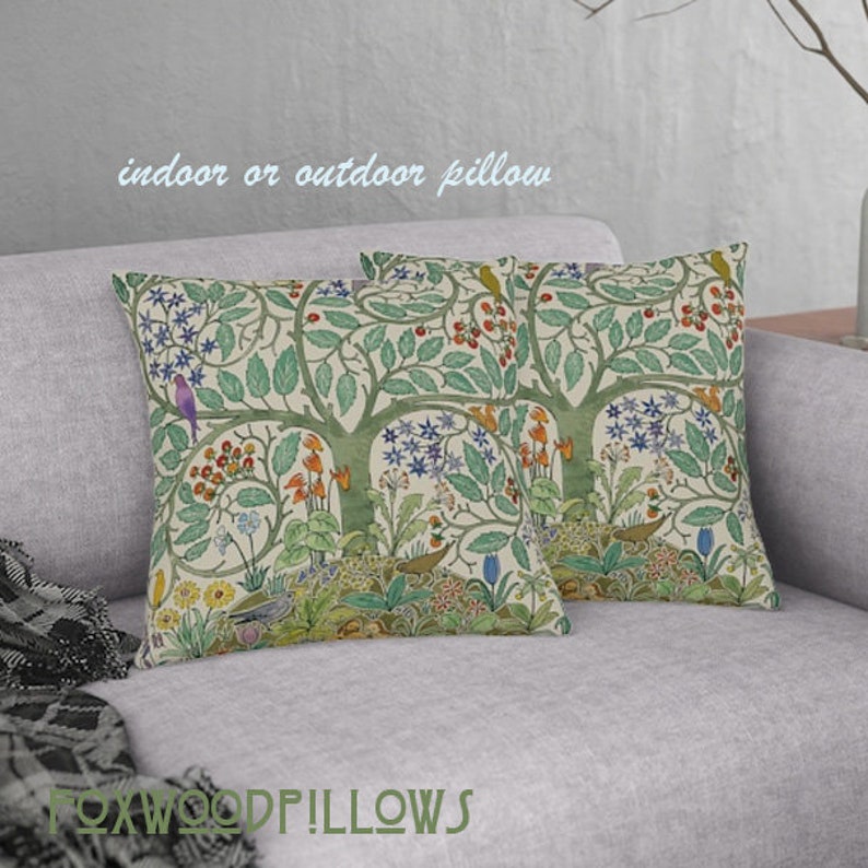 May include: Two decorative throw pillows with a floral pattern featuring a tree with birds and flowers. The pillows are on a light gray couch. The text "indoor or outdoor pillow" is visible at the top of the image.