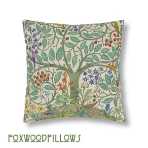 May include: A cream-colored throw pillow with a green tree and colorful flowers and birds printed on it. The pillow has a square shape and a subtle texture.