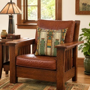 May include: A brown leather armchair with a wooden frame and vertical slat sides. A square throw pillow rests on the seat, featuring a geometric pattern in shades of green, yellow, and brown. The chair has a thick back cushion and a seat cushion.