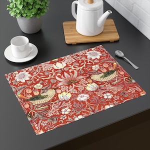 May include: Red placemat with a floral pattern featuring birds and leaves. The placemat has a white background with red, yellow, and green accents.