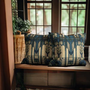 May include: Two square throw cushions featuring a geometric pattern in shades of cream, dark blue, and muted green. The design consists of vertical lines and angular shapes that create a structured, repeating motif across the fabric surface.