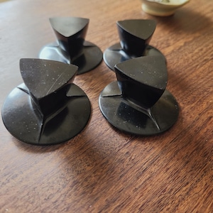 May include: A set of four black knobs, each featuring a circular base and a triangular top handle. The knobs have a smooth, solid finish and are arranged in a square formation, showcasing a functional design with clean lines and a uniform appearance.