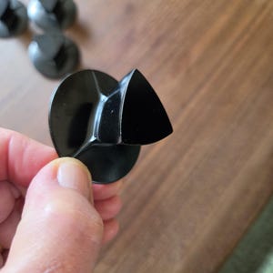 May include: A set of black plastic control knobs, each featuring a circular base and a protruding triangular grip. The knobs have a smooth, glossy finish and a distinct three-sided shape designed for manual adjustment on a compatible appliance.