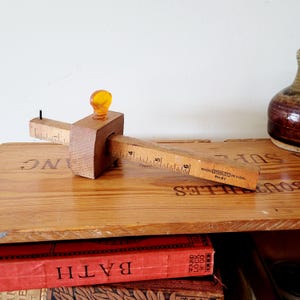 Könnte beinhalten: Ein hölzernes Streichmaß Stanley No. 61 mit einem skalierten Balken in Zoll-Einheiten. Das Werkzeug besteht aus einem zentralen Holzblock mit einer bernsteinfarbenen Kunststoff-Feststellschraube und einer kleinen Metallspitze am Ende.