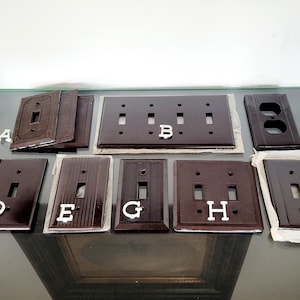 May include: A collection of dark brown electrical switch plates, each with a unique design and layout. Some plates have multiple openings for switches, while others have a single opening. The plates are labeled with white letters A through I.