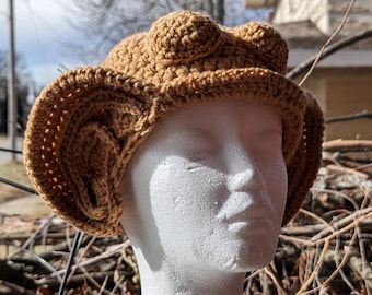 May include: A brown crocheted hat with large ear flaps. The hat is on a white mannequin head.