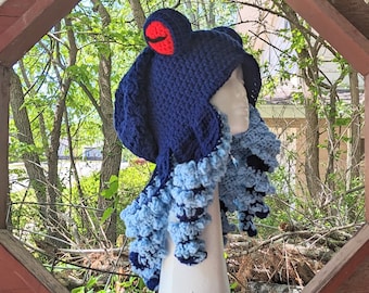 May include: A blue and light blue crocheted octopus hat with a red mouth. The hat is on a white mannequin head.