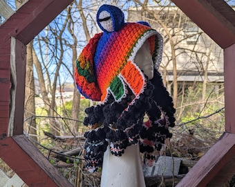 May include: A colorful crocheted hat with a rainbow pattern and a black crocheted beard. The hat is on a white mannequin head.