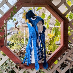 May include: A blue crocheted octopus hat with yellow tentacles. The hat is on a white mannequin head.