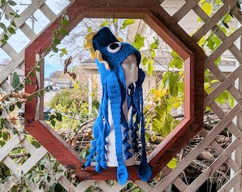 May include: A blue crocheted octopus hat with yellow tentacles. The hat is on a white mannequin head.