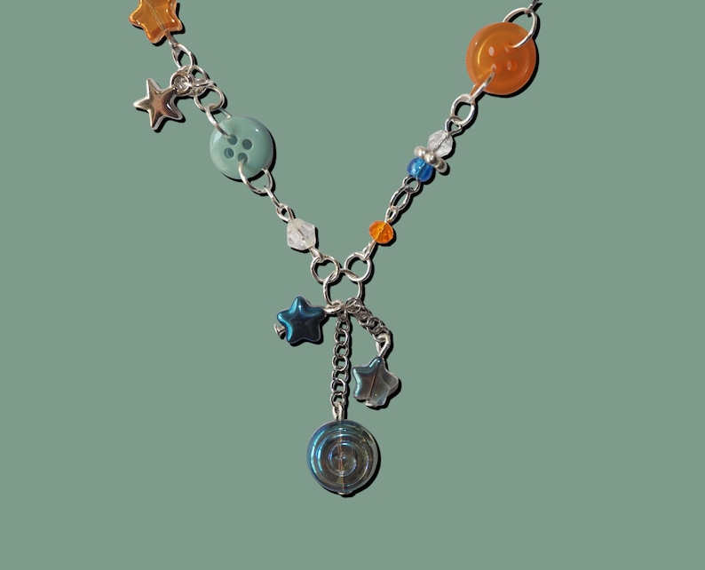 May include: A silver-toned necklace with a variety of colorful beads and charms. The necklace features orange, blue, and clear beads, along with star-shaped and button-shaped charms. A spiral charm hangs from the center.