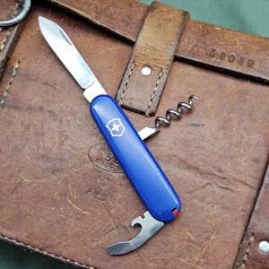 May include: A blue Swiss Army knife with a corkscrew, bottle opener, and blade. The knife is lying on a brown leather surface with the number 52019 stamped on it.