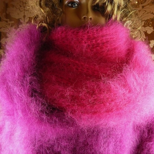 Può includere: Un maglione soffice di colore rosa acceso e vibrante, caratterizzato da un collo ad anello spesso e oversize. Il capo è realizzato in un materiale a maglia testurizzata a pelo lungo che crea un aspetto morbido e voluminoso.