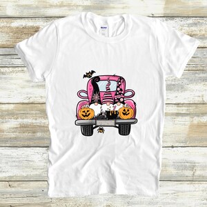 May include: Three gnomes in a pink pickup truck with pumpkins and a cauldron. The gnomes are wearing witch hats and have black beards. The truck has black wheels and a black spider on the back.