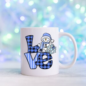 Pu&ograve; includere: Tazza in ceramica bianca con la scritta "LOVE" in motivi a quadri e righe blu. Un pupazzo di neve dei cartoni animati con cappello e sciarpa blu tiene in mano un fiocco di neve. La tazza ha un manico bianco ed &egrave; ambientata su uno sfondo azzurro sfocato.