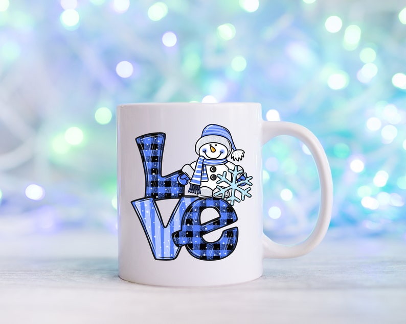 Pu&ograve; includere: Tazza in ceramica bianca con la scritta "LOVE" in motivi a quadri e righe blu. Un pupazzo di neve dei cartoni animati con cappello e sciarpa blu tiene in mano un fiocco di neve. La tazza ha un manico bianco ed &egrave; ambientata su uno sfondo azzurro sfocato.
