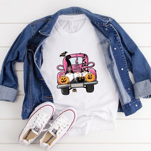 May include: A white t-shirt with a pink truck carrying three gnomes with pumpkins. The gnomes are wearing hats and have beards. There are bats flying around the truck.
