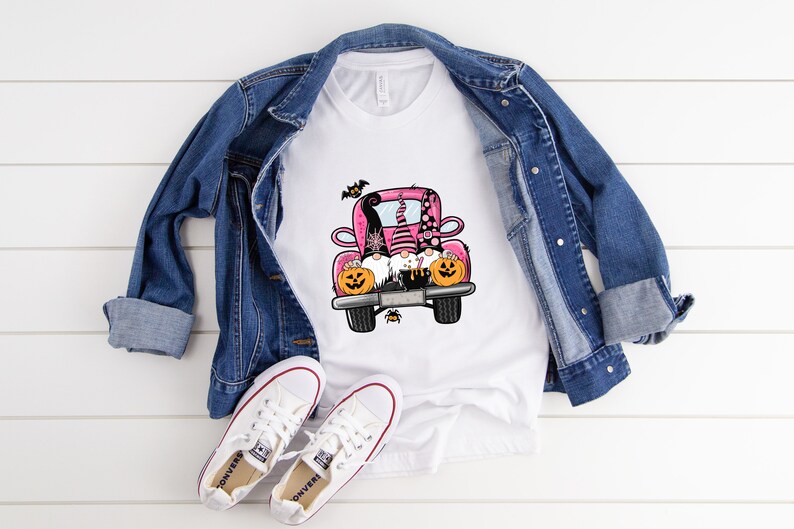 May include: A white t-shirt with a pink truck carrying three gnomes with pumpkins. The gnomes are wearing hats and have beards. There are bats flying around the truck.
