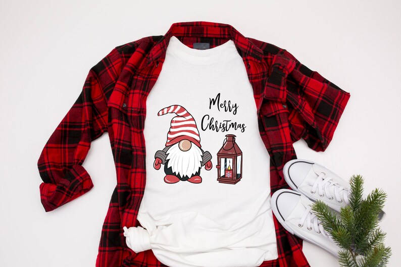 May include: White t-shirt with a Christmas gnome graphic and the words "Merry Christmas". The gnome wears a red and white striped hat and mittens. A red and black plaid shirt and white sneakers are also in the image.
