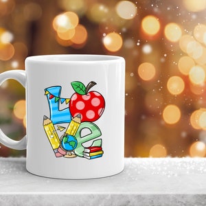 May include: White ceramic mug with a colorful illustration of the word "LOVE" made up of school supplies, including pencils, a globe, and a red apple.