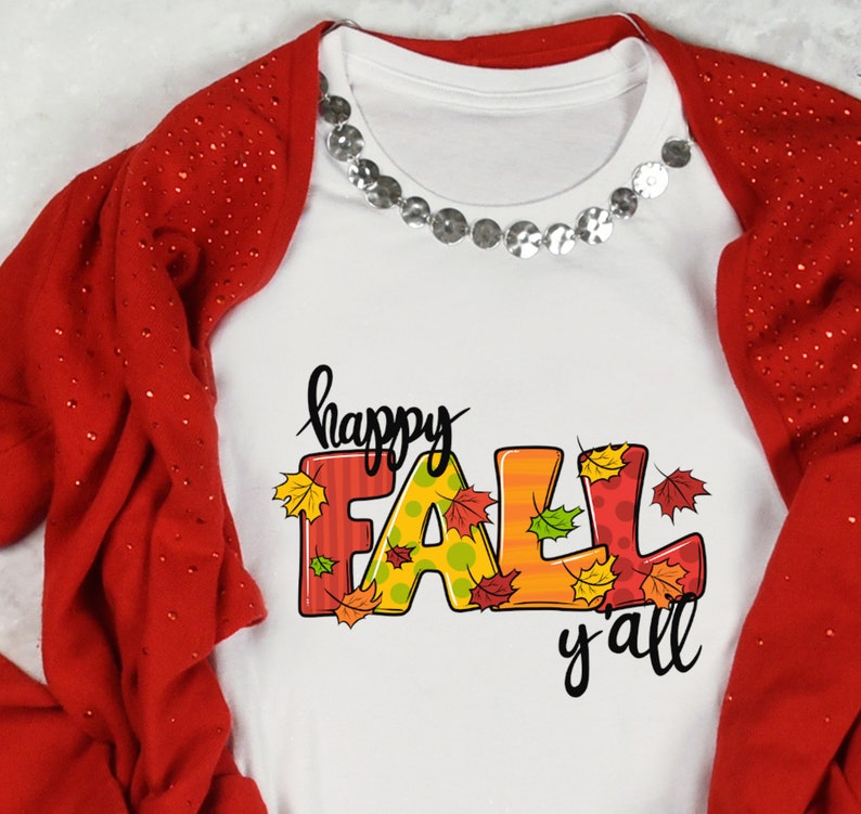 May include: White t-shirt with the words "happy FALL y'all" in black script and colorful block letters. The letters are decorated with fall leaves. A red cardigan with sparkly details is draped over the shirt.