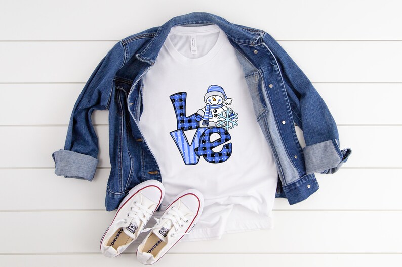 Pu&ograve; includere: Maglietta bianca con scritta "love" a quadri blu e pupazzo di neve con fiocco di neve. Sono presenti anche una giacca di jeans blu e scarpe da ginnastica bianche. Il tema &egrave; abbigliamento casual invernale.
